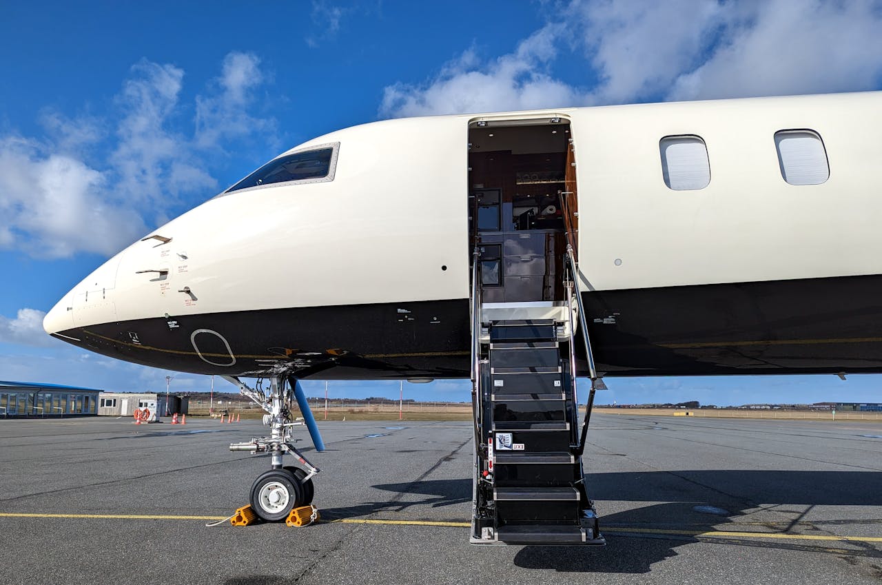 A private jet with an open door, parked on an airport ramp under a clear blue sky.